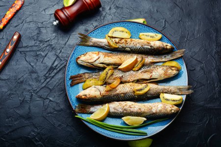 Téléchargez les photos : Délicieux petit poisson grillé entier avec kiwi et sauce citron vert dans une assiette. - en image libre de droit
