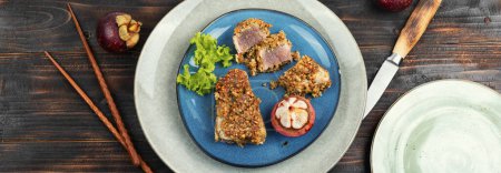 Téléchargez les photos : Steak de thon cuit dans une panique aux noix avec un mangoustan sur une table rustique en bois. Pose plate. - en image libre de droit