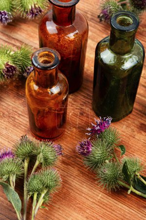 Foto de Planta de bardana sobre fondo de madera y pequeña botella de vidrio con tinturas, hierbas medicinales - Imagen libre de derechos