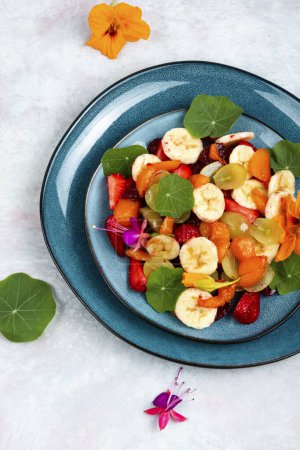 Foto de Ensalada de frutas con vitaminas frescas con plátano, fresas, uvas y capuchina. Puesta plana. - Imagen libre de derechos
