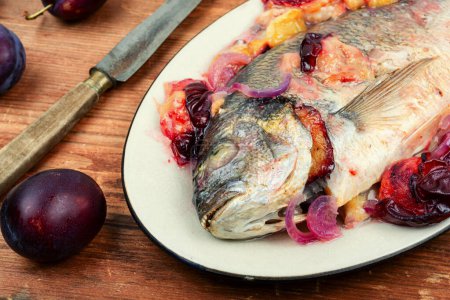 Téléchargez les photos : Dorado poisson cuit avec des prunes. Dorado rôti entier sur table en bois. - en image libre de droit