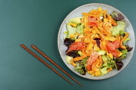 Téléchargez les photos : Salade fraîche avec saumon, mangue, sésame et légumes. Salade et baguettes - en image libre de droit
