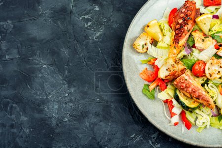 Téléchargez les photos : Salade saine de légumes et poulpe grillé dans une assiette sur une table en pierre noire. Espace pour le texte - en image libre de droit