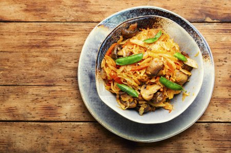 Téléchargez les photos : Chou savoureux cuit avec des champignons et des carottes. Nourriture carême sur table rustique en bois - en image libre de droit