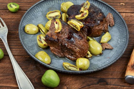 Photo for Dish of ostrich steak roasted with mini kiwi sauce. Meat with kiwi berries on wooden table. - Royalty Free Image