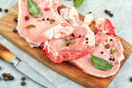 Téléchargez les photos : Steak de porc frais cru dans des épices sur une planche de bois. De la viande. Porc aux côtes. - en image libre de droit