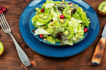 Téléchargez les photos : Salade végétalienne de kiwi, légumes verts, baies et pignons de pin sur table en bois. Repas santé. - en image libre de droit