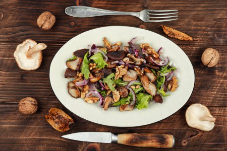 Foto de Ensalada con champiñones asados, cebollas, lechuga y nueces. Comida vegetariana saludable en mesa de madera negra. Estilo rústico. - Imagen libre de derechos