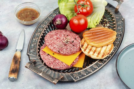 Téléchargez les photos : Galettes de hamburger frais, fromage, légumes et petits pains pour la cuisine. Côtelettes de steak crues à la viande hachée. - en image libre de droit