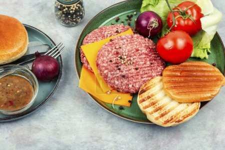 Foto de Hamburguesas frescas, queso, verduras y bollos de hamburguesas para cocinar. Chuletas de carne cruda con carne picada. - Imagen libre de derechos