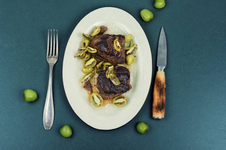 Téléchargez les photos : Steak d'autruche rôti et mini kiwi dans une assiette - en image libre de droit