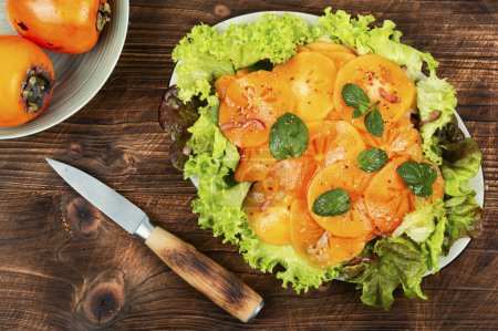 Photo for Autumn persimmon salad with green lettuce and mint on wooden table. Healthy vegetarian food. - Royalty Free Image