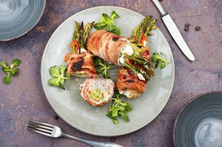 Photo for Grilled meat rolls wrapped in bacon with green young asparagus on a plate. Top view. - Royalty Free Image