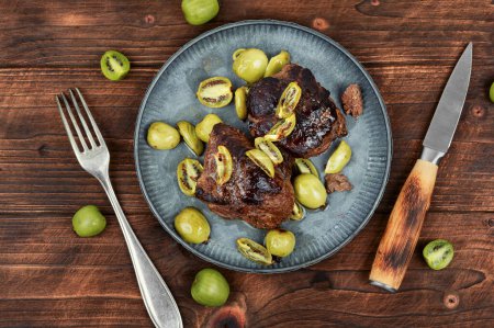 Téléchargez les photos : Plat de steak d'autruche rôti avec mini sauce kiwi. Viande aux baies de kiwi sur table en bois. - en image libre de droit