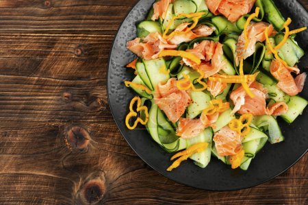Téléchargez les photos : Salade fraîche avec saumon fumé et concombre frais servi sur une assiette noire sur un vieux fond en bois. Cuisine asiatique. - en image libre de droit