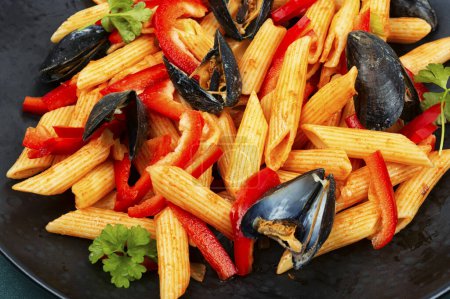 Téléchargez les photos : Macaroni aux moules sur une assiette sombre. Pâtes méditerranéennes aux fruits de mer. Gros plan. - en image libre de droit