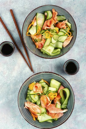 Photo for Fresh Asian salad with smoked salmon, fresh cucumber and chopstick. Top view. - Royalty Free Image