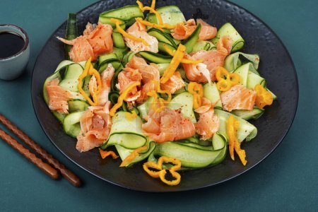Téléchargez les photos : Salade asiatique au saumon fumé et concombre frais servi sur une assiette noire. - en image libre de droit