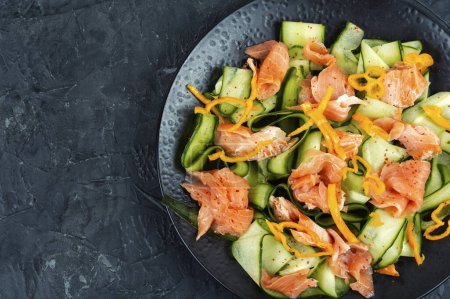 Téléchargez les photos : Délicieuse salade de saumon fumé et concombre frais servie sur une assiette noire. Espace pour le texte. - en image libre de droit