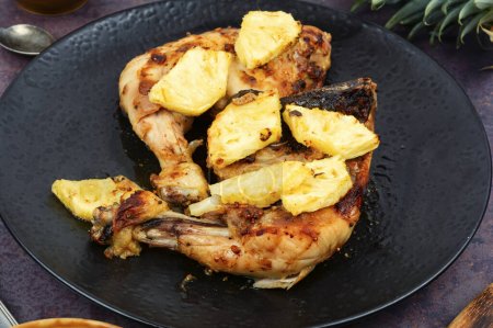 Hühnerkeulen mit Ananasstücken gegrillt. Gebackenes Hühnerfleisch auf einem schwarzen Teller.
