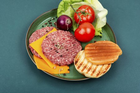 Téléchargez les photos : Galette de hamburgers crus juteux, fromage, légumes et petits pains pour la cuisine. Côtelettes de steak crues à la viande hachée. - en image libre de droit