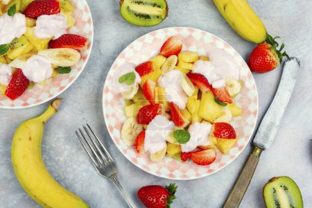 Photo for Summer fruit salad of pineapple, strawberries, kiwi and yogurt on a plate. Making fruit salad. - Royalty Free Image