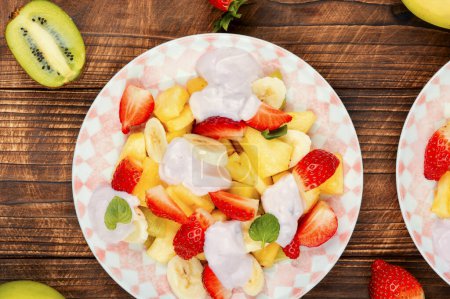 Téléchargez les photos : Salade de fruits maison d'ananas, fraises, kiwi et yaourt sucré sur une vieille table rustique en bois. - en image libre de droit