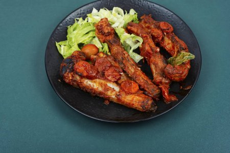 Téléchargez les photos : Côtes de porc braisées ou cuites dans une sauce tomate servie dans une assiette sombre. BBQ. - en image libre de droit