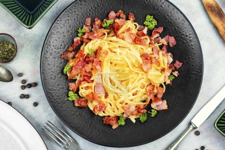 Téléchargez les photos : Pâtes Carbonara avec bacon et parmesan servi sur une assiette noire. Cuisine italienne traditionnelle. Pose plate. - en image libre de droit