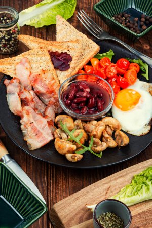 Téléchargez les photos : Petit déjeuner anglais : œufs frits, bacon, légumes, haricots et pain grillé dans une assiette. - en image libre de droit
