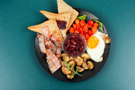 Photo for English breakfast: fried egg, fried bacon,vegetables, beans and toast on a plate. - Royalty Free Image