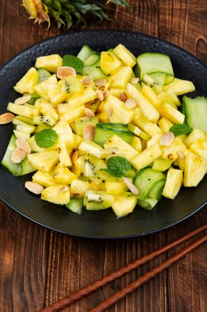 Téléchargez les photos : Salade tropicale végétalienne d'ananas frais et de concombre sur une vieille table rustique en bois. - en image libre de droit
