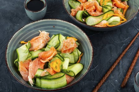 Téléchargez les photos : Salade de printemps fraîche au saumon fumé, concombre sur une table de cuisine en béton. Cuisine asiatique. - en image libre de droit