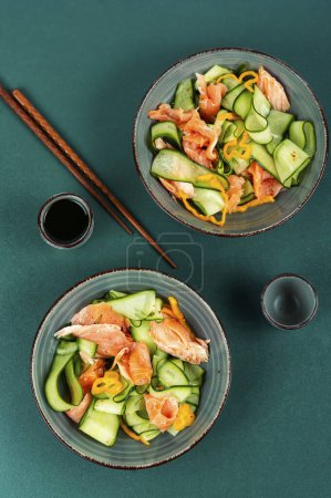 Asian spicy salad with salted salmon fillet, fresh cucumbers and chopstick. Flat lay.