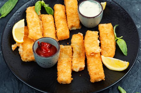 Crumbed fried fish fingers in sticks with sauce. Close up.