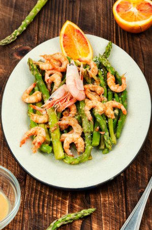 Roast asparagus with fried prawns on rustic wooden table.