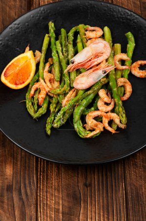 Roast asparagus spears with fried prawns on rustic wooden table.