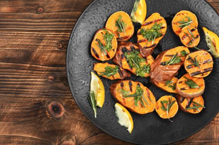 Photo for Barbecue grilled sweet potato, batata with herbs on a vintage wooden background. Copy space. - Royalty Free Image
