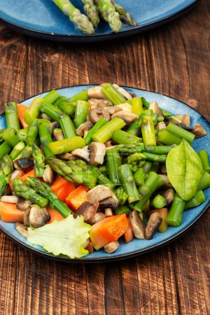 Photo for Dietary vegetarian salad of green asparagus and fried mushrooms on a wooden table. - Royalty Free Image