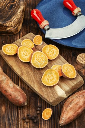 Sweet potato, board and knife. Fresh sweet potatoes or batatas on a vintage wooden background. Dietary food.