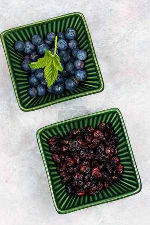 Photo for Ceramic bowl of fresh blueberries and dried cranberries. Healthy food. Flat lay. - Royalty Free Image