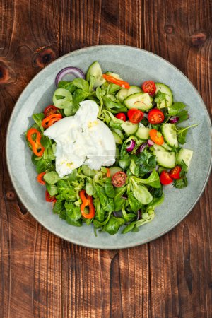 Photo for Salad of greens, tomatoes, cucumbers and fresh cream cheese Burrata. Burrata salad with vegetables on rustic wooden table - Royalty Free Image