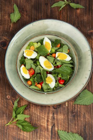 Photo for Homemade green salad with nettles, tomatoes and eggs on a wooden background. Ukrainian food. - Royalty Free Image