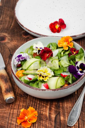 Foto de Ensalada saludable hecha de verduras frescas y decorada con flores comestibles en una mesa de madera rústica. - Imagen libre de derechos