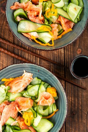 Photo for Homemade Asian salad with smoked salmon and fresh cucumber on old rustic wooden table. Flat lay. - Royalty Free Image