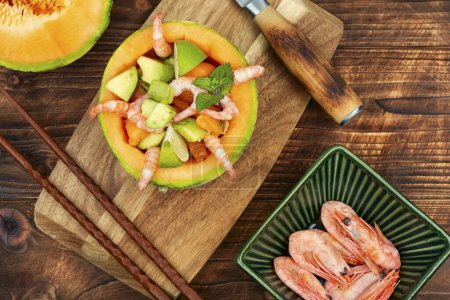 Asian salad of melon, shrimp and avocado on wooden table. Flat lay.