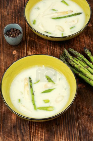 Dietary vegetarian soup with white and green asparagus on rustic wooden table.