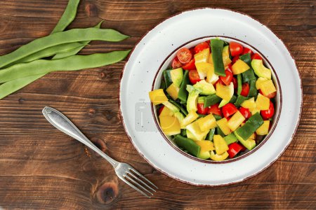 Foto de Vegetable salad with bell pepper, tomato, avocado and runner beans in bowl on rustic wooden table. Rustic style. - Imagen libre de derechos