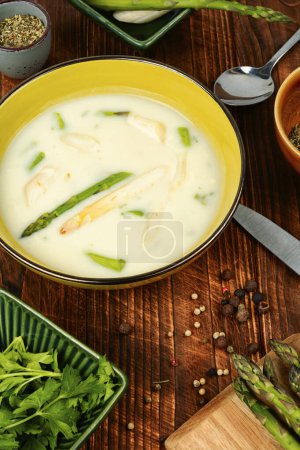 Dietary vegetarian soup puree with white and green asparagus on rustic wooden table.