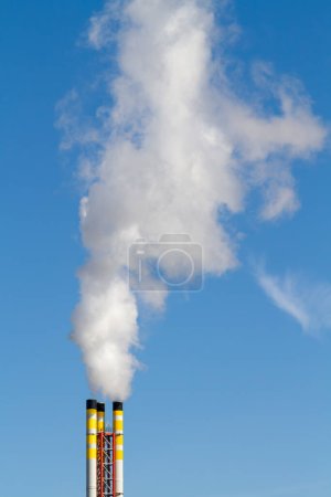Foto de Chimenea de un incinerador de residuos que emite humo y contamina el aire contra un cielo azul claro. - Imagen libre de derechos